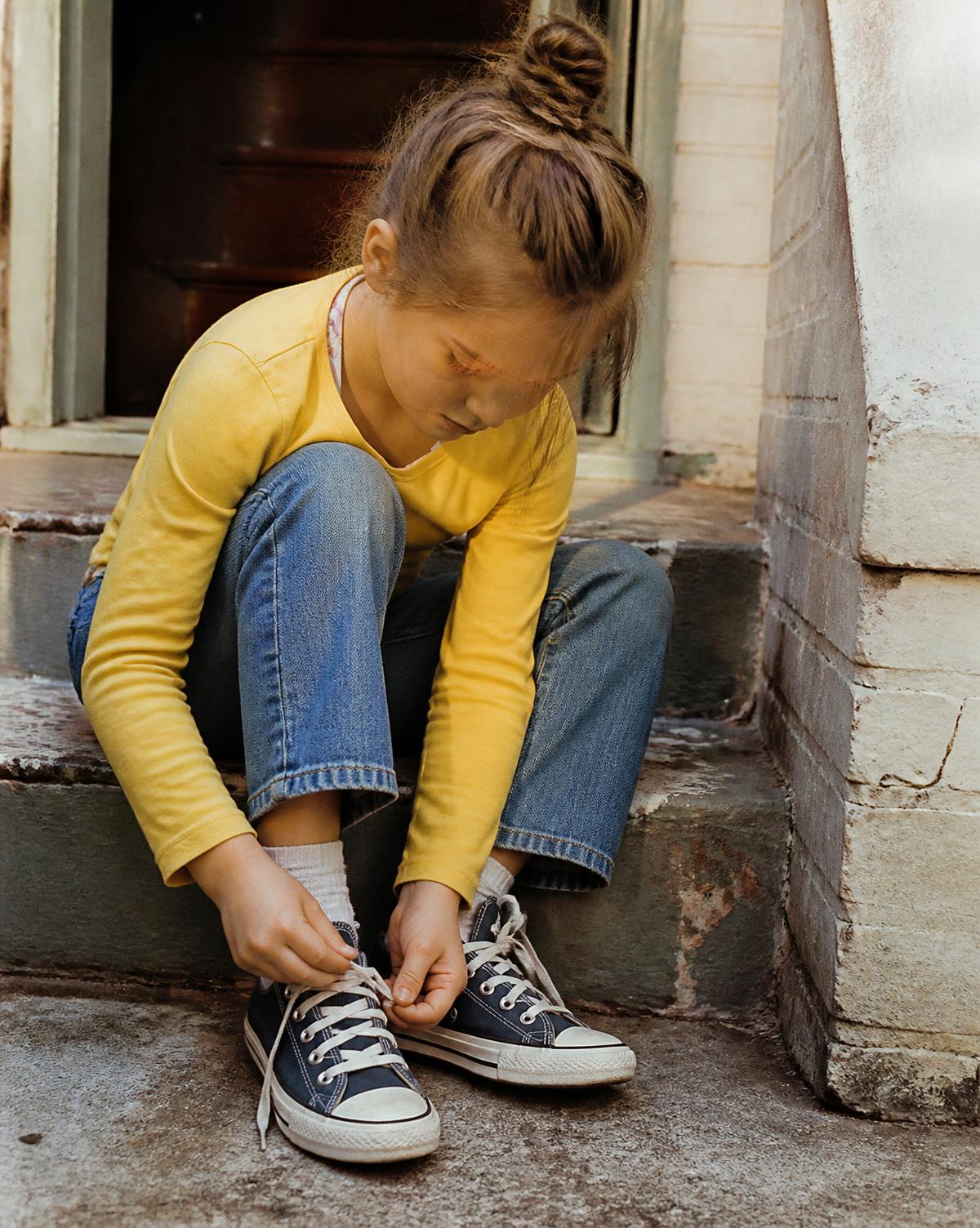 A child sitting on a doorstep, tying their own shoes